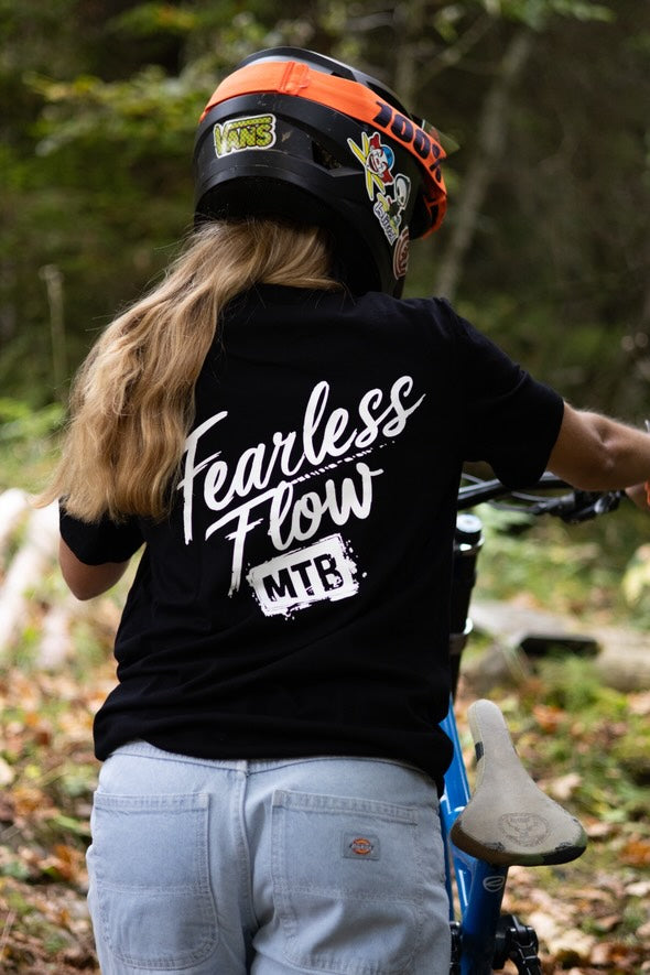 Hoodie noir Fearless Flow pour rider VTT freeride, porté par l’ambassadrice Mathilde pousse son DH Commencal au bike park, vue de dos.