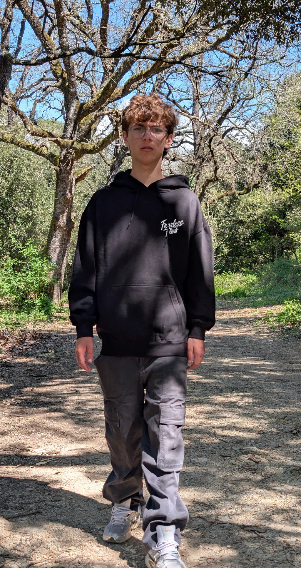 Hoodie streetwear VTT Fearless Flow noir avec logo brodé poitrine, porté en extérieur sur un sentier en forêt