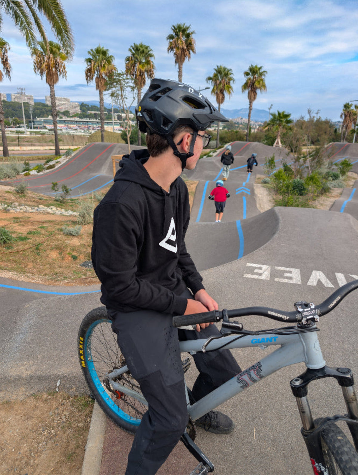 sweat à capuche VTT noir Fearless Flow pour rider VTT freeride, porté par l’ambassadeur Timéo assis sur son dirt au pump park de Cagnes-sur-Mer, vue de face.
