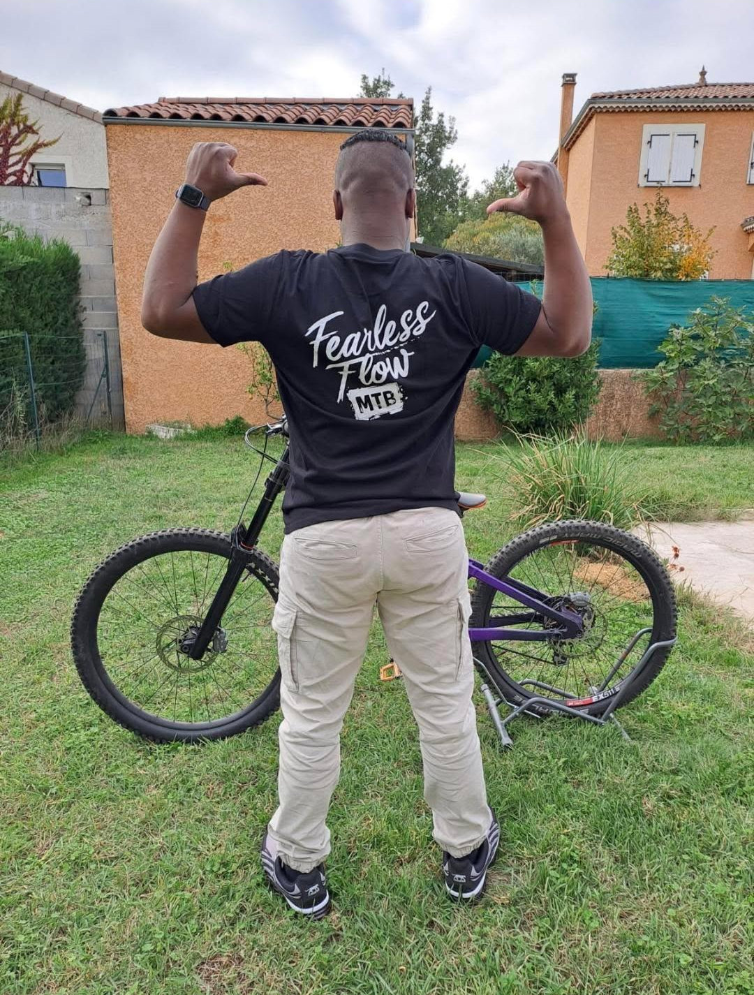 Hoodie noir Fearless Flow pour rider VTT freeride, porté par l’ambassadeur Corentin devant son DH Marin violet, vue de dos.