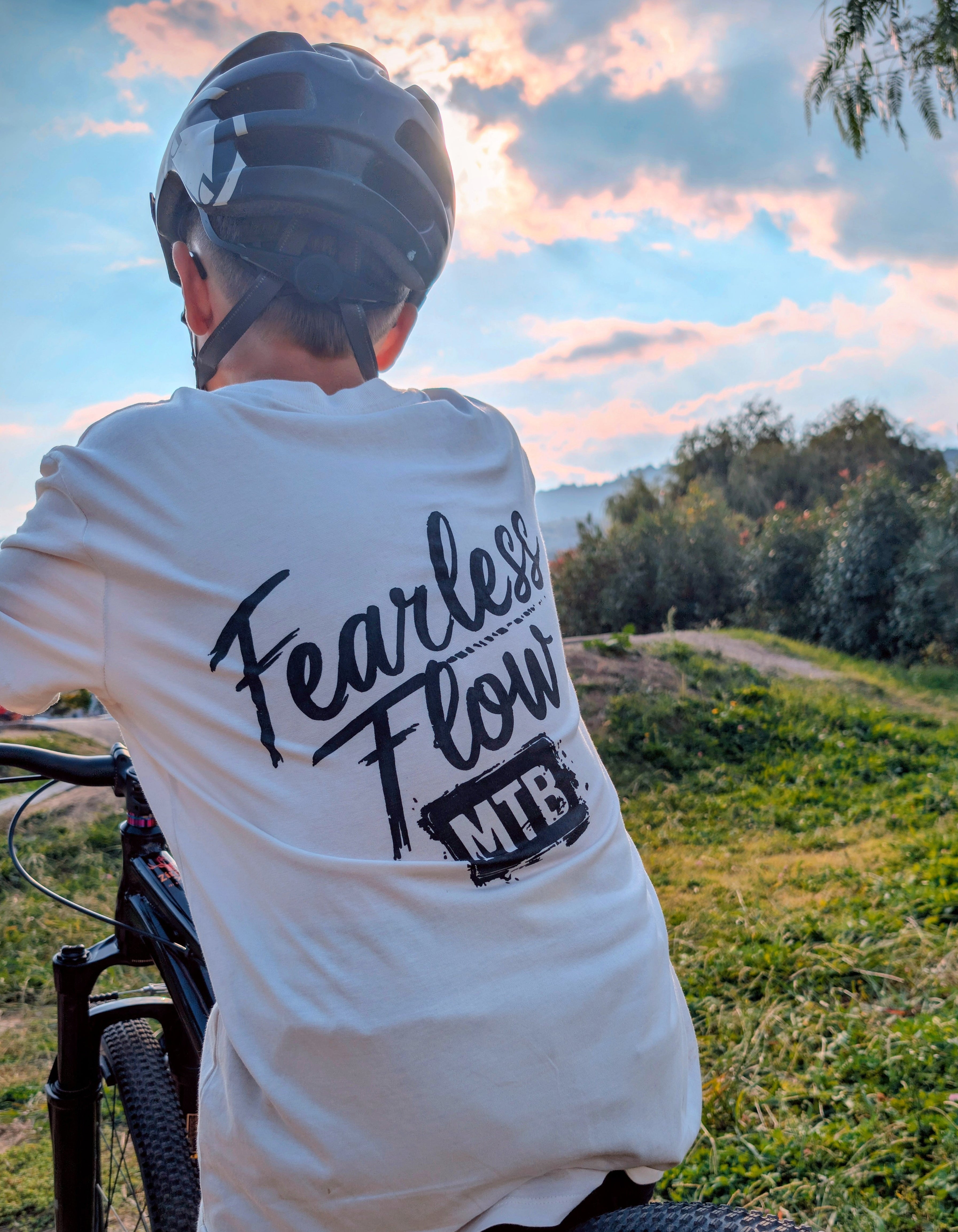 Tee-shirt écru Fearless Flow pour rider VTT freeride, porté par l’ambassadeur Nélio, vue de dos avec inscription noire.
