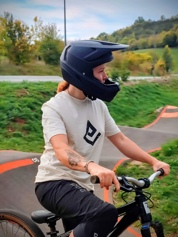 T-shirt écru Fearless Flow pour rider VTT freeride, porté par l’ambassadrice Melissa sur son dirt au pump park, vue de face avec logo noir.