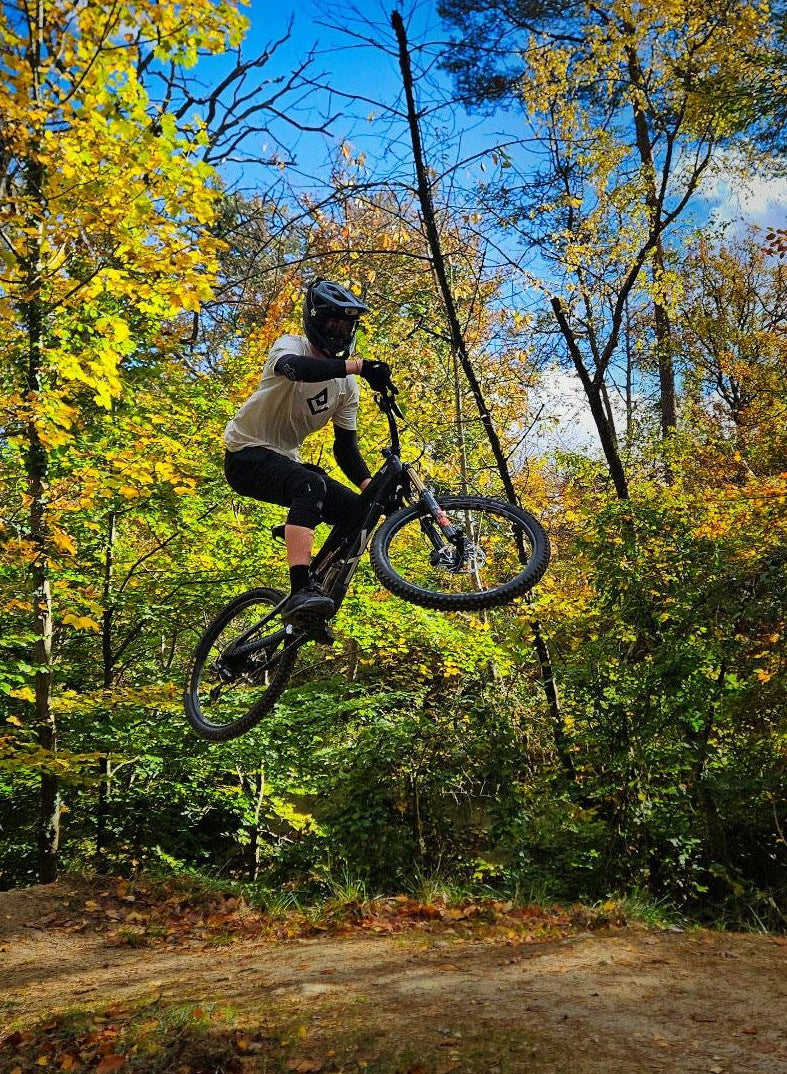 Tee-shirt écru Fearless Flow pour rider VTT, freeride, vue de face logo impression noire, porté par l'ambassadeur Mathis en train de faire un saut avec son VTT.